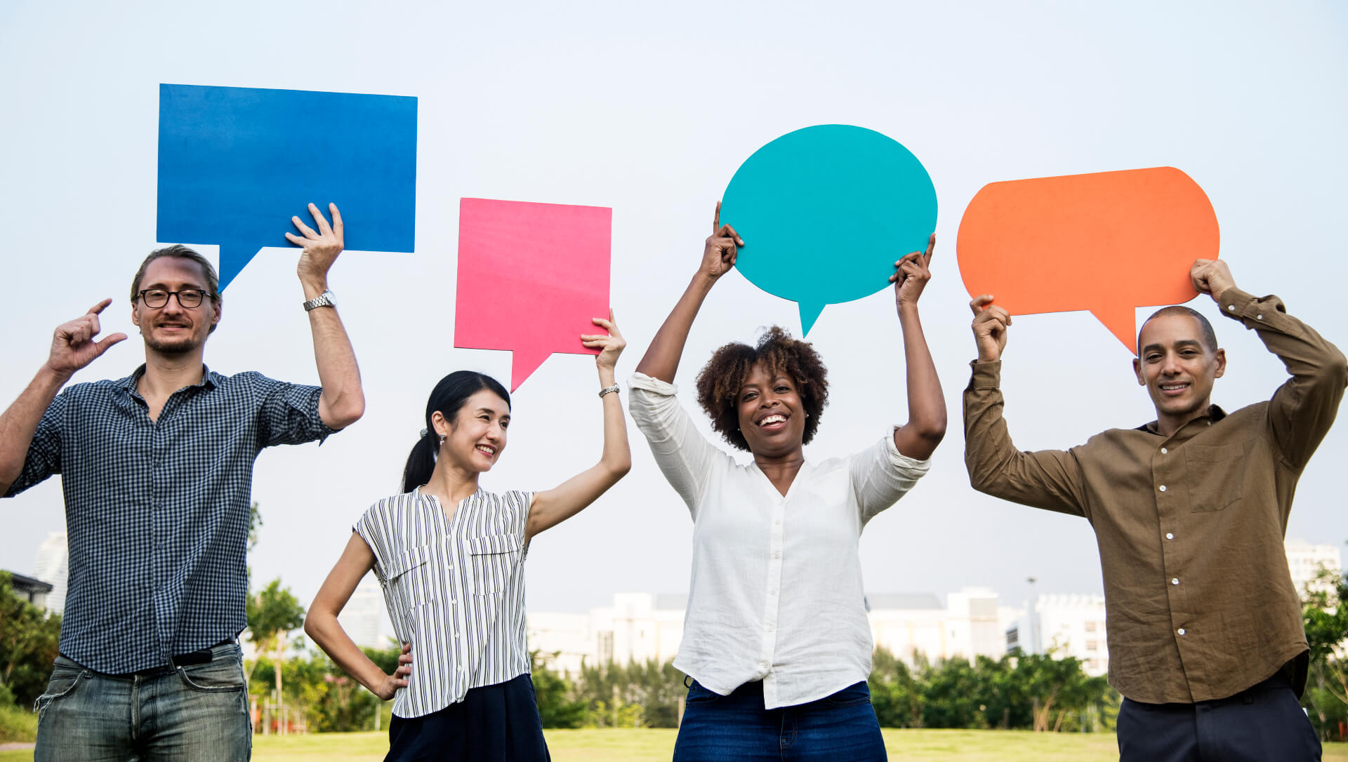 Four smiling people from different backgrounds standing outdoors, each holding a colourful speech bubble above their head