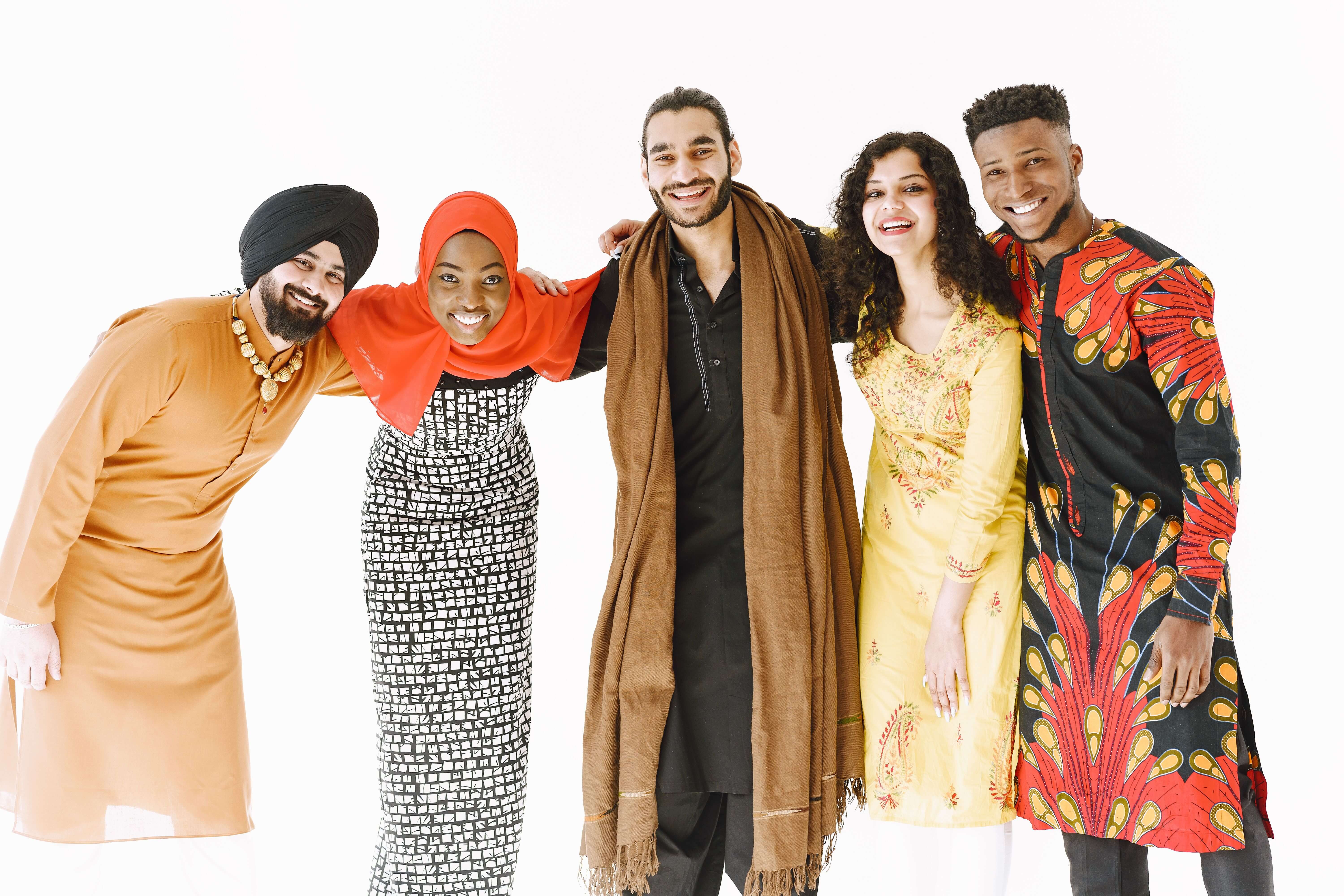 Five smiling friends of African and South Asian heritage standing arm in arm, wearing colourful traditional clothing